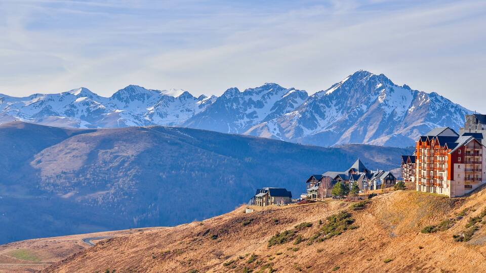 A mountainous landscape with snow-capped peaks and a cluster of traditional buildings on a hillside.