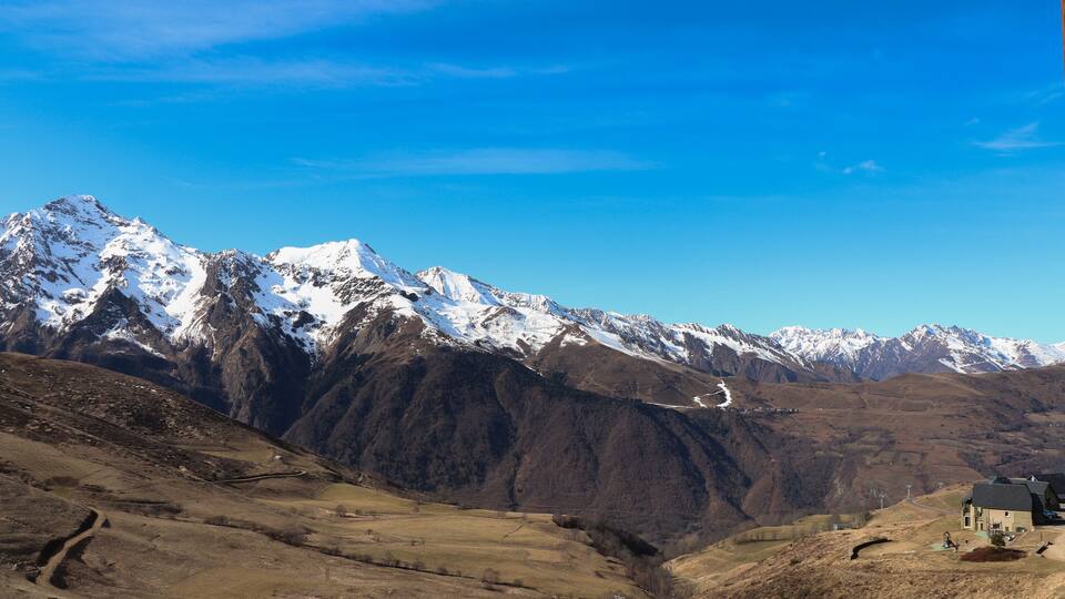 A mountainous landscape with snow-capped peaks, a winding road, and a small building.