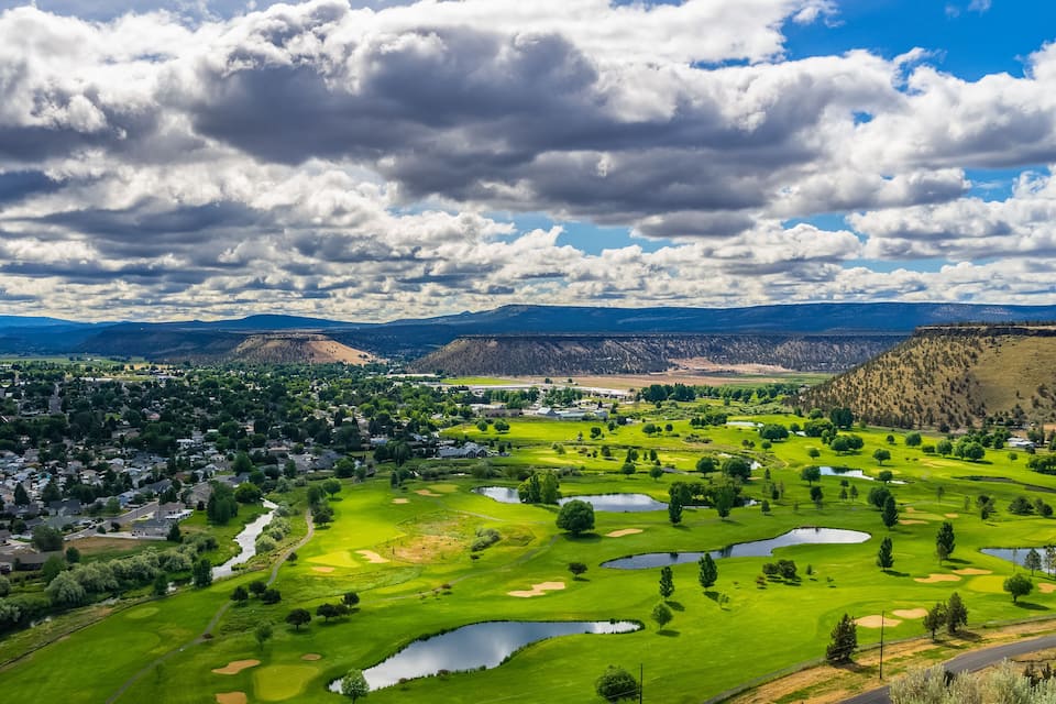 A golf course with ponds, surrounded by residential areas and mountains.