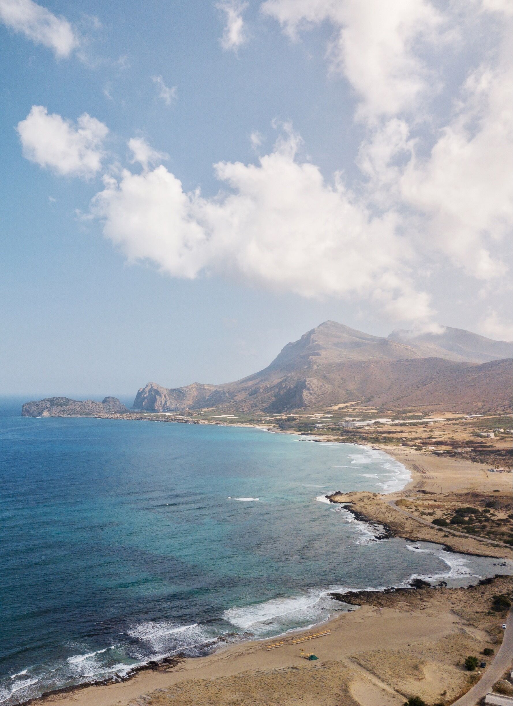 A coastal landscape with a clear sky, a sandy beach, and a mountain in the background.