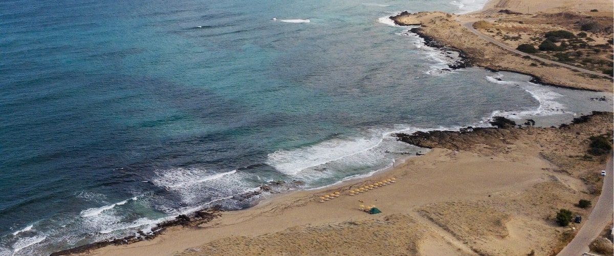 A coastal landscape with a clear sky, a sandy beach, and a mountain in the background.