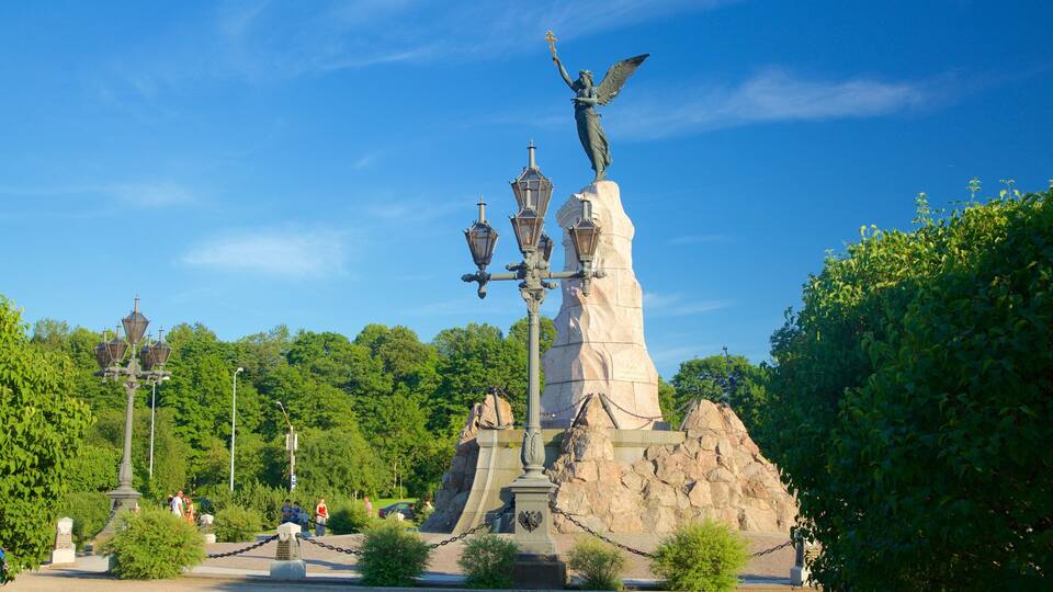 A statue of an angel with a cross, surrounded by a stone monument and a chain-link fence.