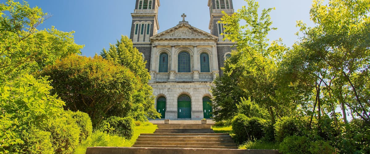 A historic church with twin towers and a central dome, surrounded by lush greenery.