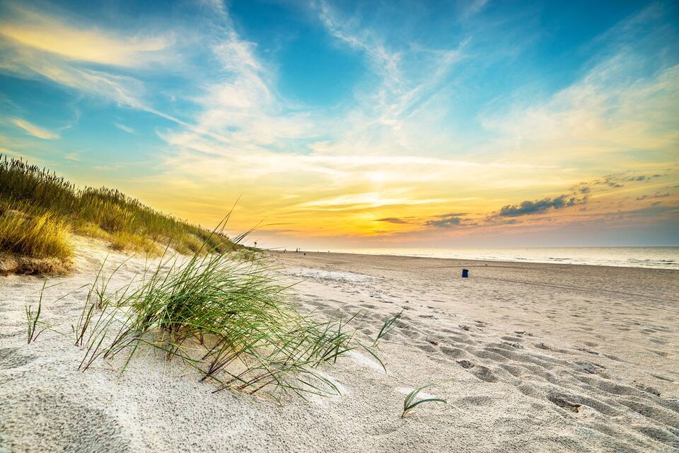 A beach with sand dunes and a sunset.