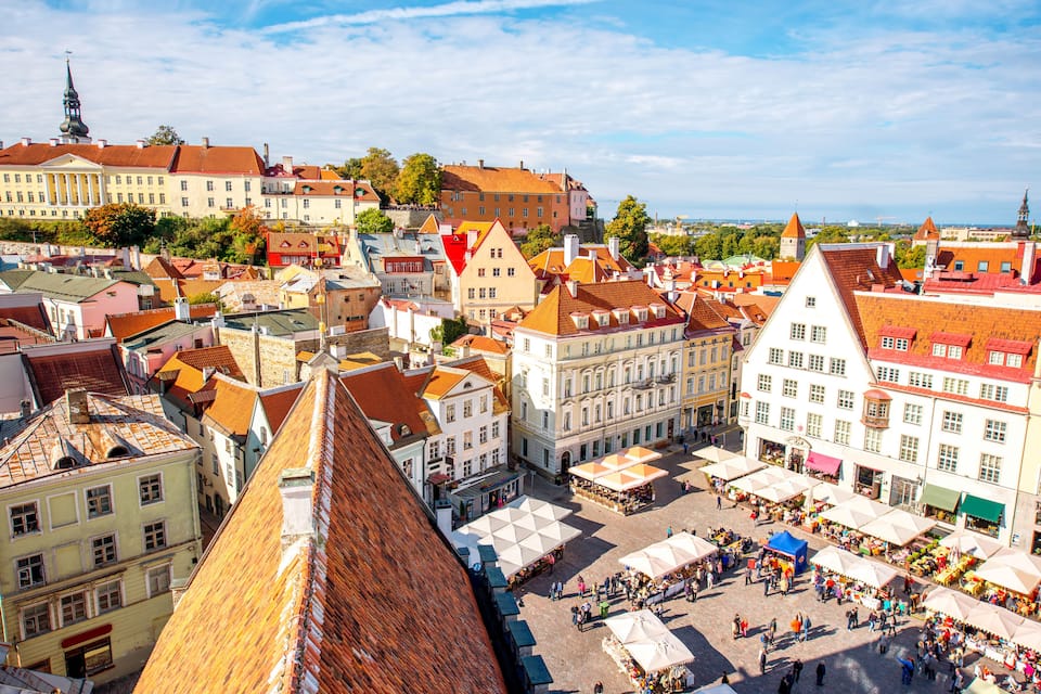 A bustling European market square surrounded by historic buildings with red-tiled roofs.