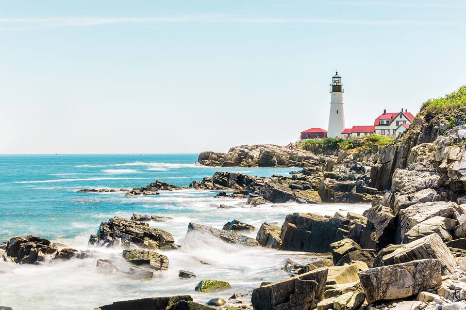 A rocky coastline with a lighthouse and houses.