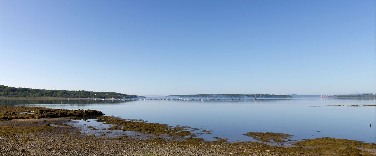 A calm lake with boats, rocky shore, and distant hills.