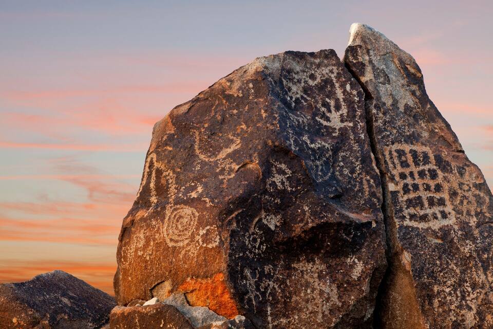 Une grande formation rocheuse ornée de sculptures visibles, avec un ciel au coucher du soleil.