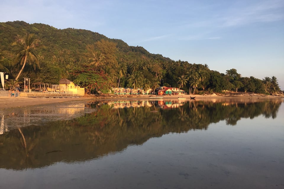 Un río tranquilo que refleja edificios y palmeras, con una colina al fondo.