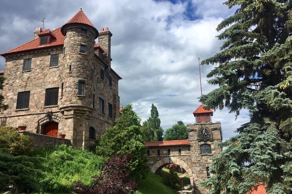 A stone castle with red-tiled roofs, a stone bridge, and lush greenery.