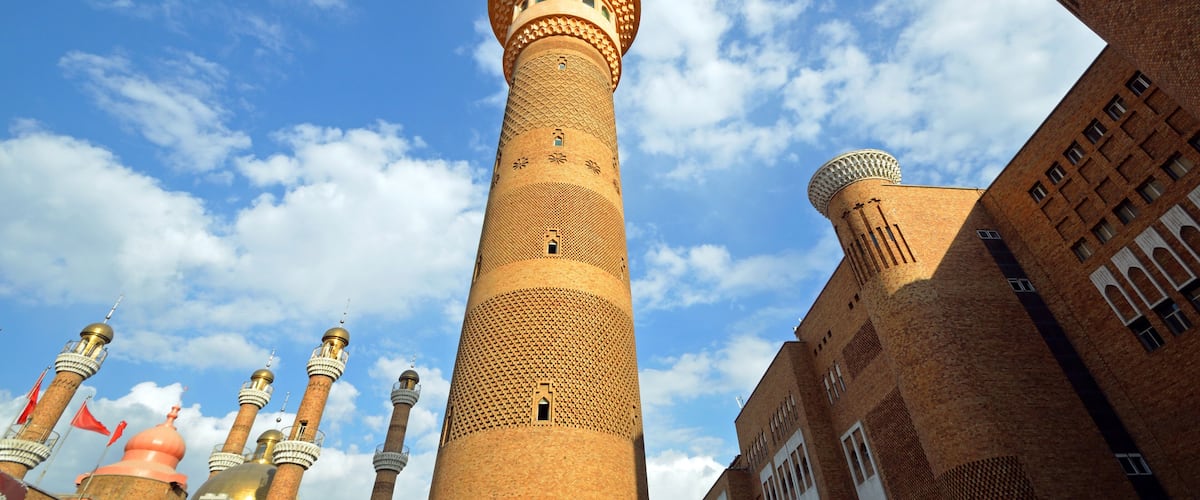 A tall brick minaret with a dome, surrounded by other buildings with similar architectural features.