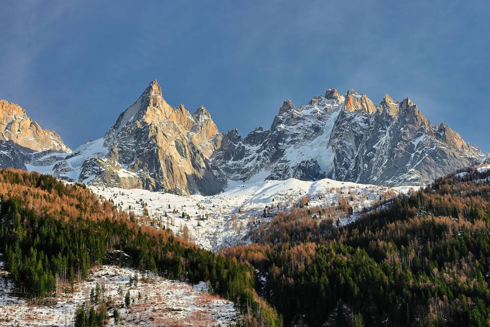 Une chaîne de montagnes aux sommets enneigés et une vallée boisée.