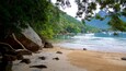 A beach with a wooden dock, rocky shoreline, and boats in the water.