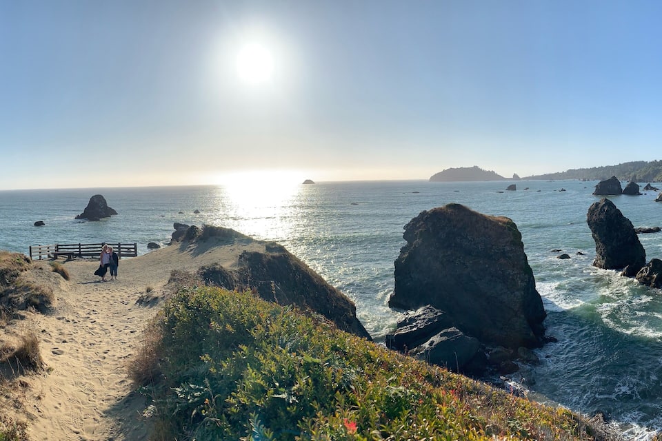 A coastal landscape with a sandy beach, rocky outcrops, and a wooden walkway.