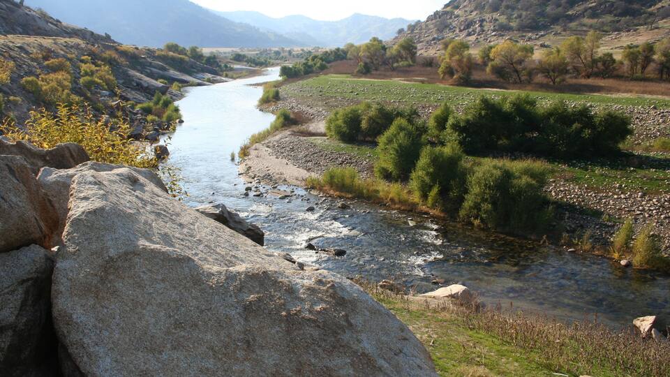 A river flowing through a valley with rocky terrain and sparse vegetation.