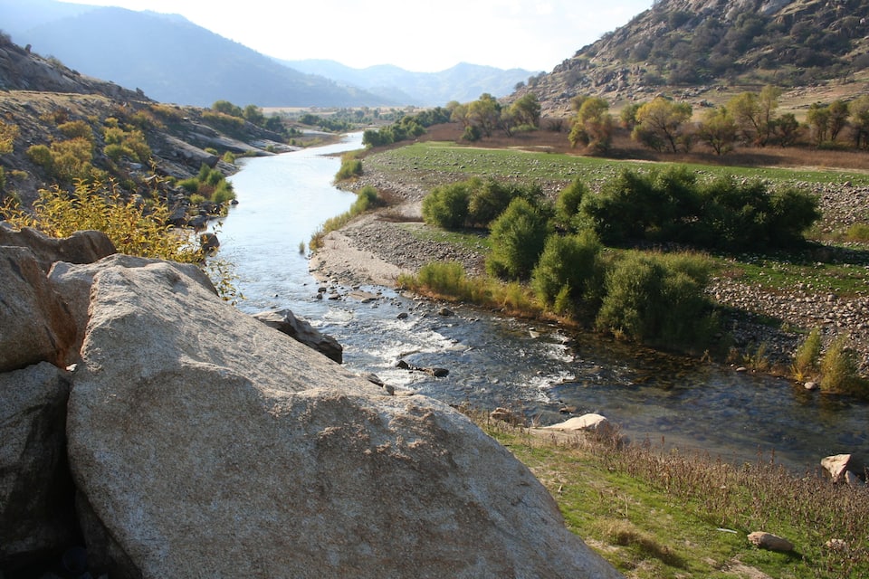 A river flowing through a valley with rocky terrain and sparse vegetation.