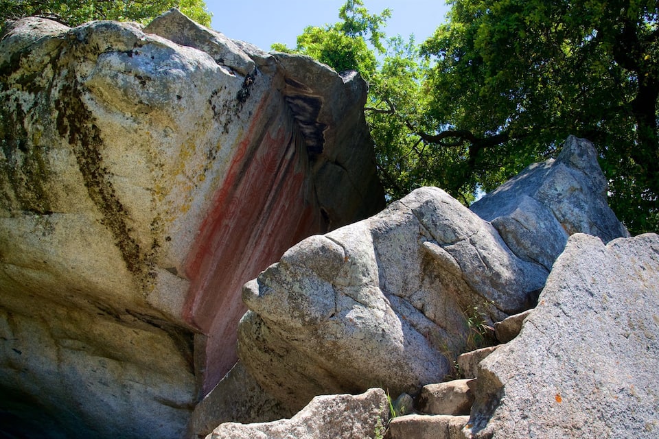 A large rock formation with a red painted area and surrounding trees.