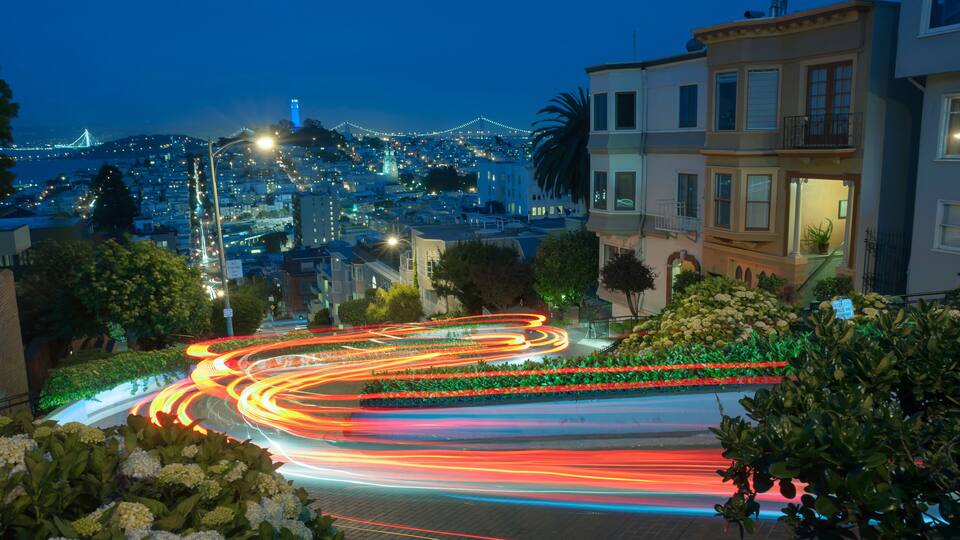 A nighttime cityscape with illuminated streets, a bridge, and residential buildings.