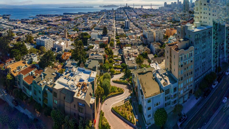A cityscape with a prominent bridge, dense urban buildings, and a coastline.