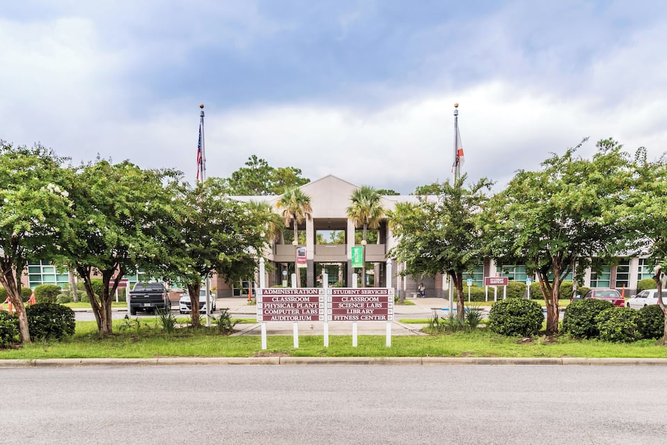 A building with flags, surrounded by trees and a sign listing facilities like classrooms and a fitness center.