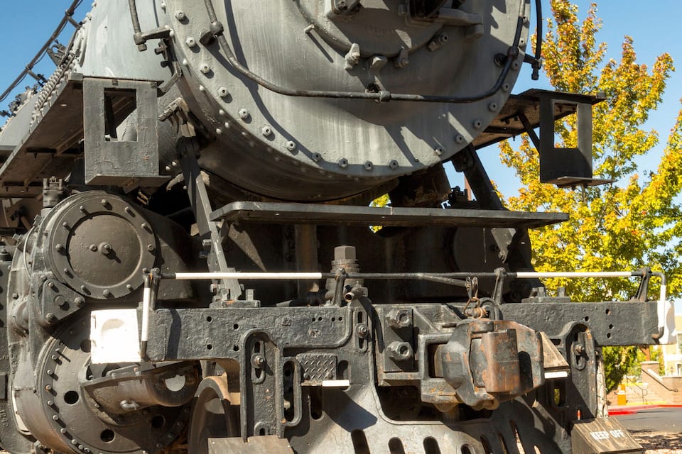 A large, vintage steam locomotive with a prominent headlight, detailed mechanical components, and a track.