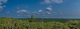 A forested landscape with a clear blue sky and scattered clouds.