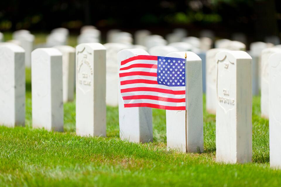 A row of white gravestones with one featuring an American flag.