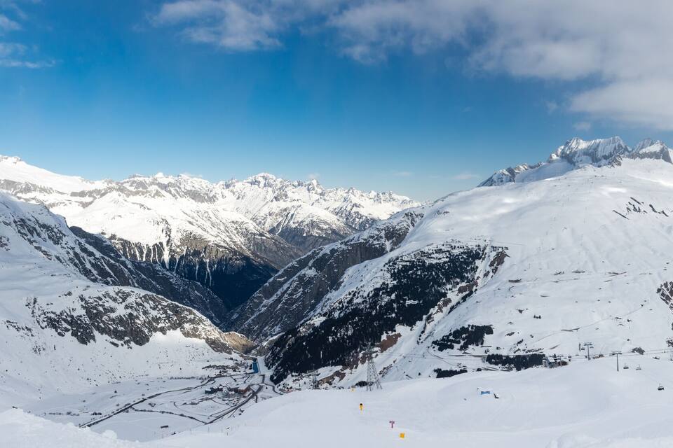 A snow-covered mountain range with ski slopes and a clear blue sky.