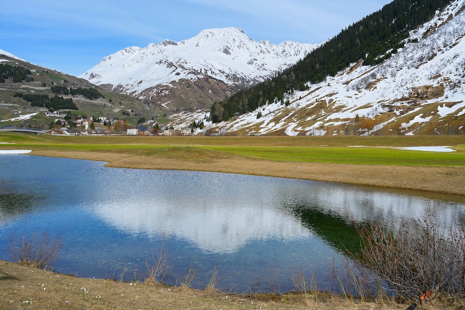 Um lago tranquilo rodeado por montanhas nevadas e uma pequena aldeia.
