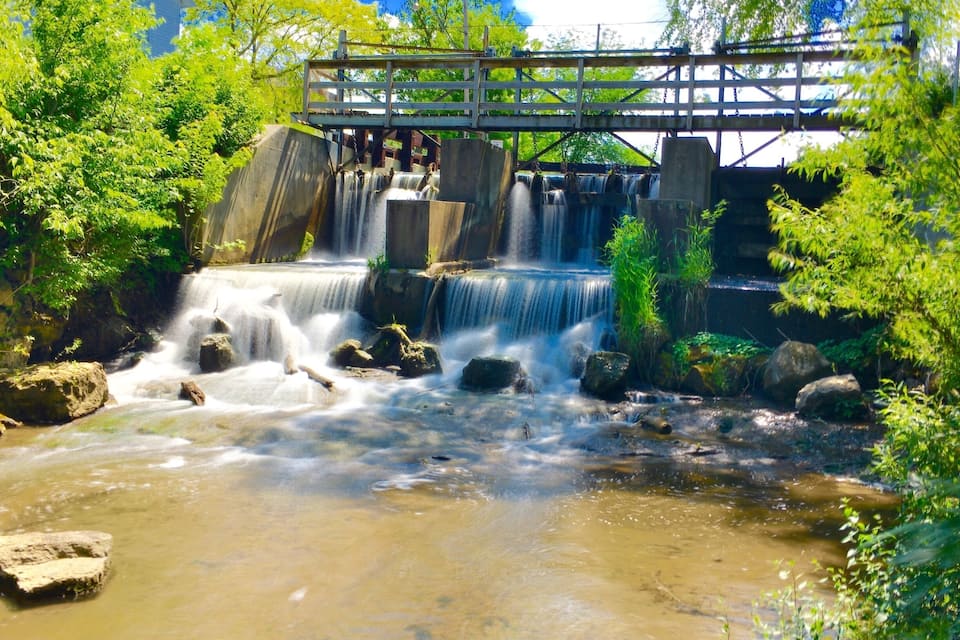 A waterfall cascading over rocks in a forested area with a wooden bridge overhead.