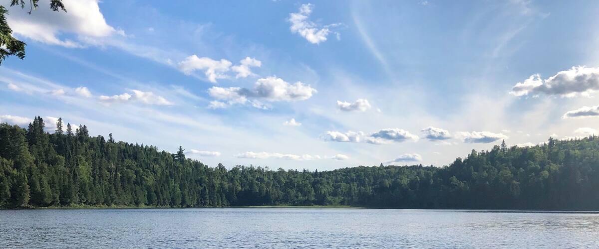 A calm lake with a forested shoreline under a partly cloudy sky.