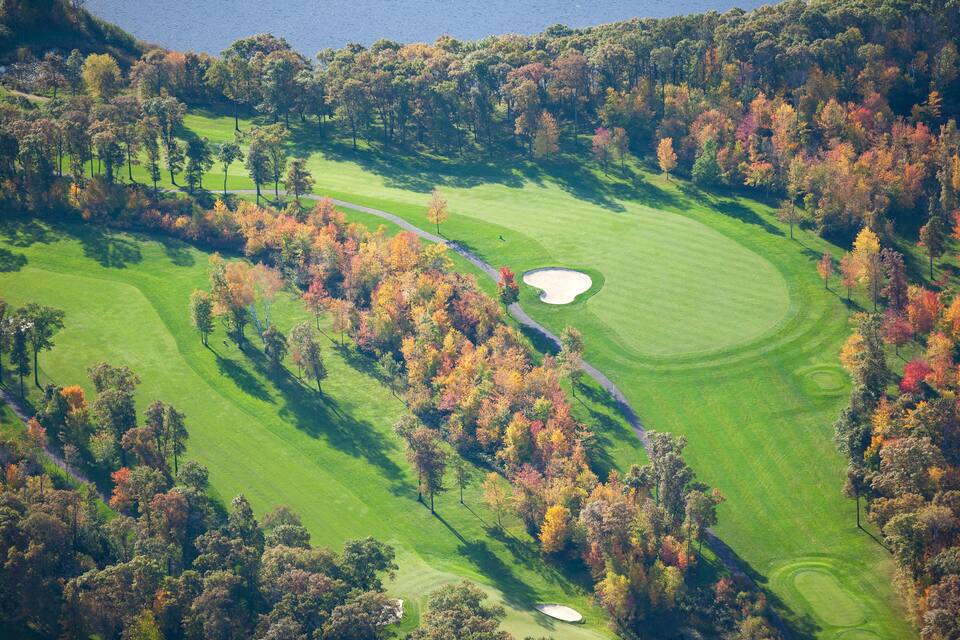 Vista aèria d'un camp de golf envoltat d'arbres de tons tardans i una massa d'aigua.