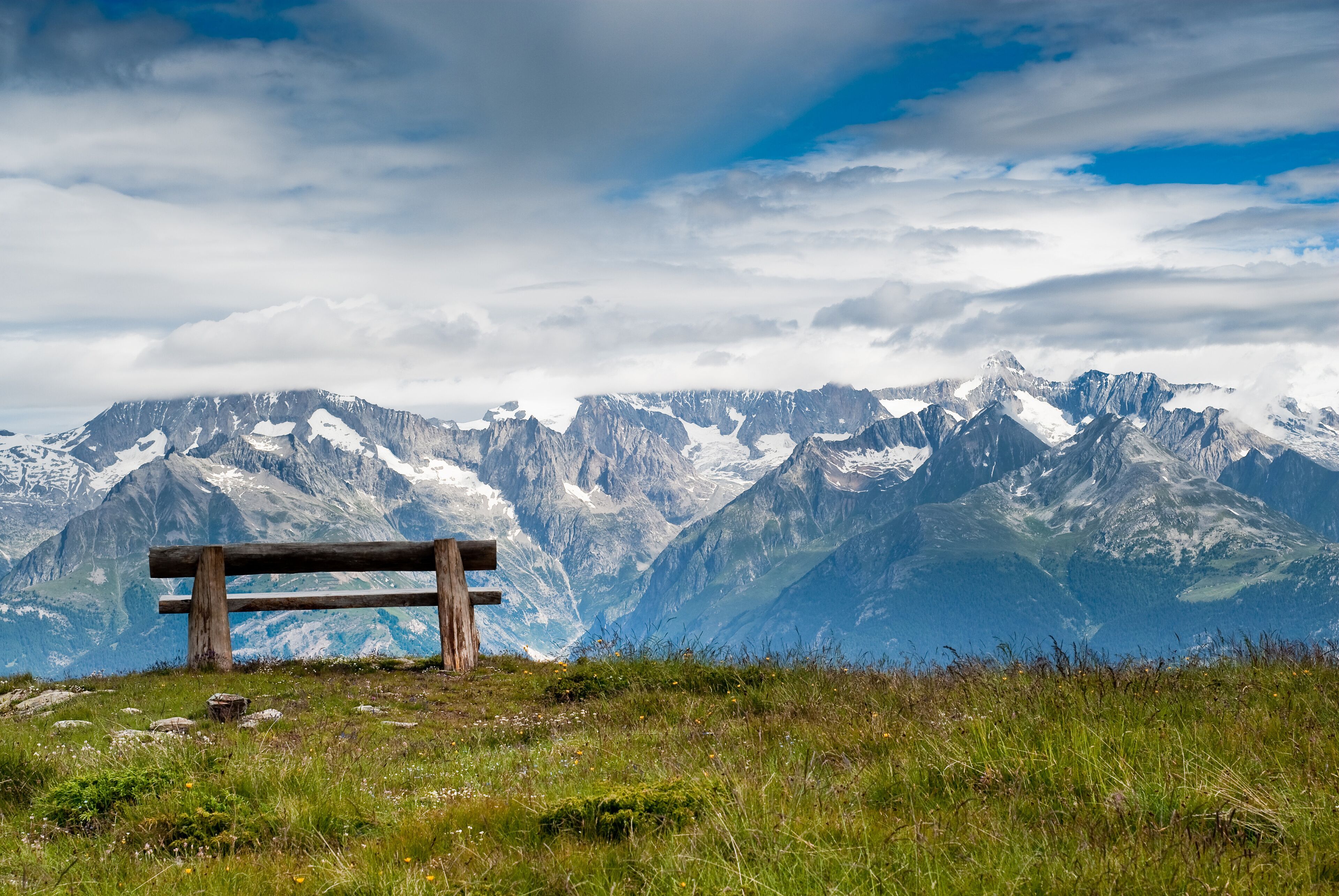 A wooden bench overlooking a mountain range with snow-capped peaks.