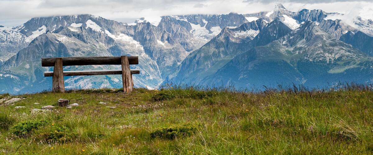 A wooden bench overlooking a mountain range with snow-capped peaks.