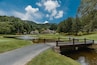Un parcours de golf avec un étang, un pont en bois et un club-house en arrière-plan.