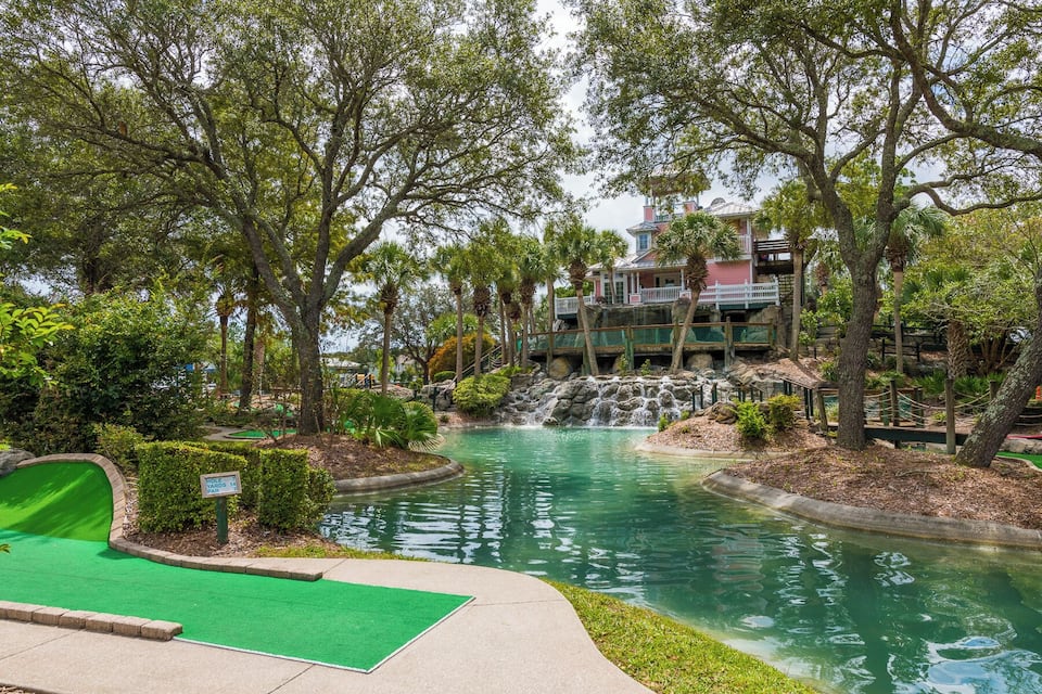 A golf course with a pond, trees, and a building with a waterfall.