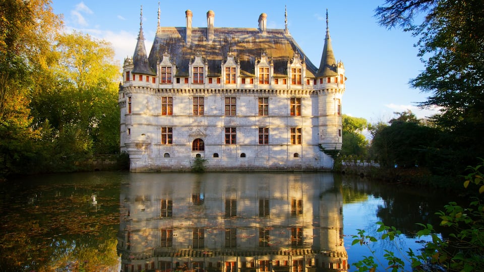 A historic castle with multiple towers, a moat, and a reflection in the water.