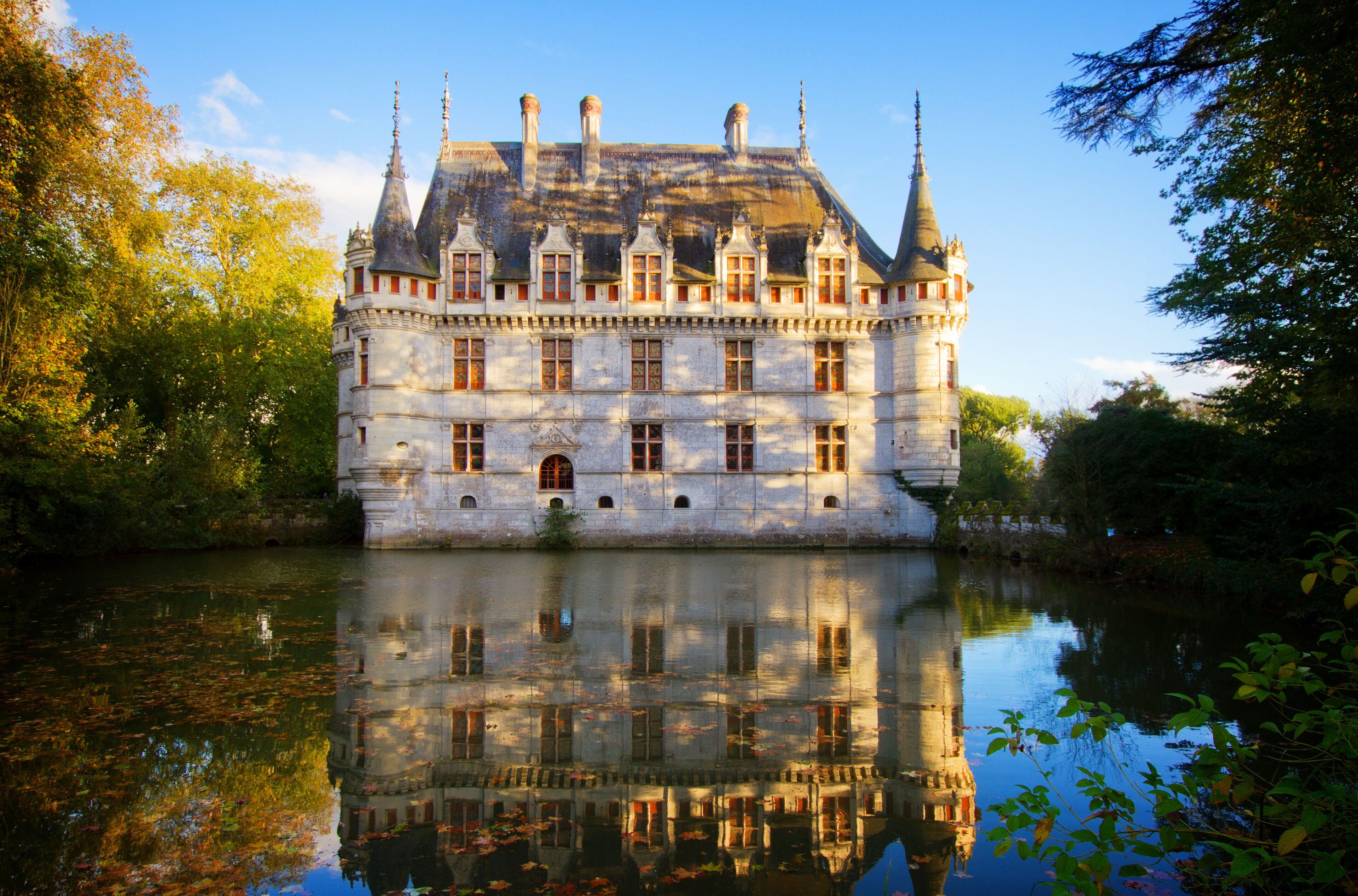 A historic castle with multiple towers, a moat, and a reflection in the water.