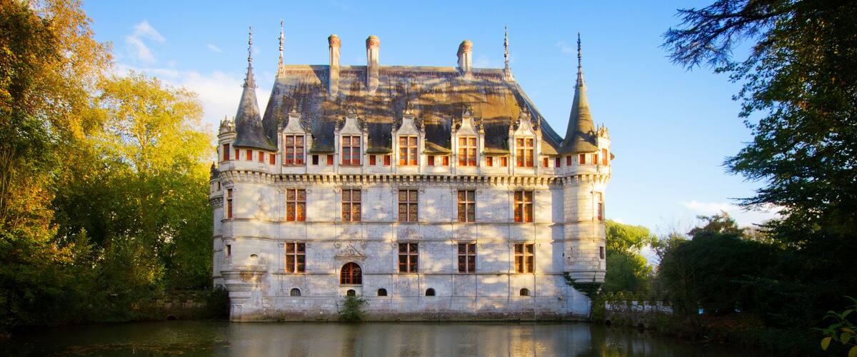 A historic castle with multiple towers, a moat, and a reflection in the water.