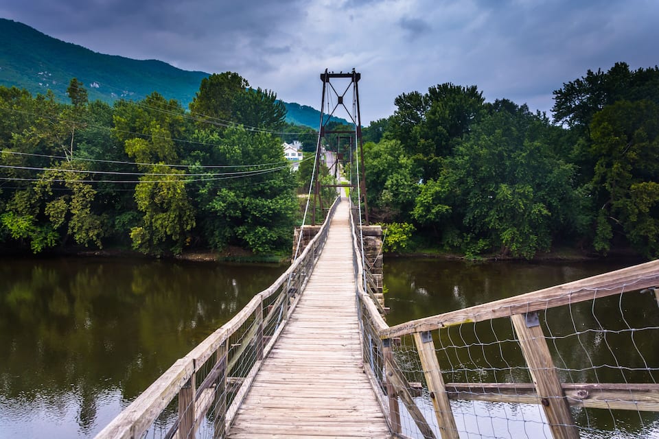 Un pont de fusta sobre un riu, amb una forest densa a ambdós costats i una muntanya al fons.