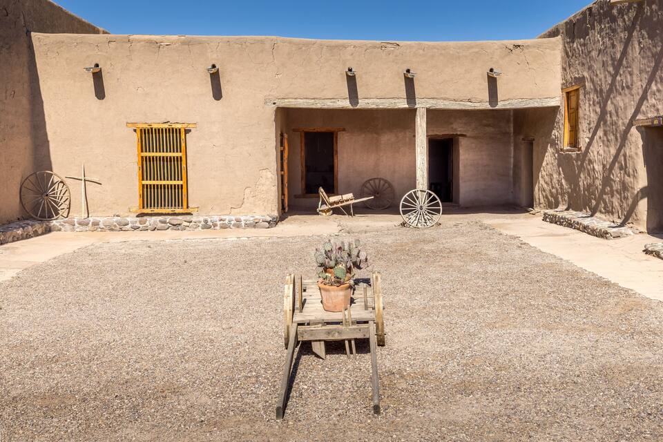 Un edificio tradicional de adobe con carretillas de madera y una maceta con cactus en el patio.