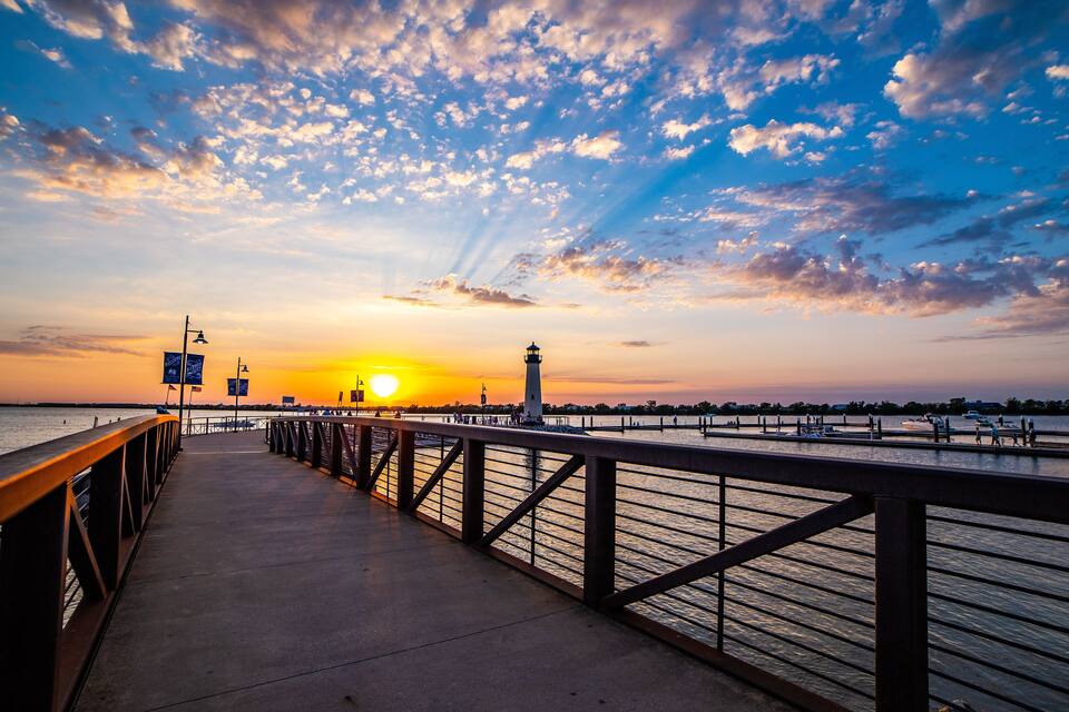 A waterfront promenade at sunset with a lighthouse and boats.