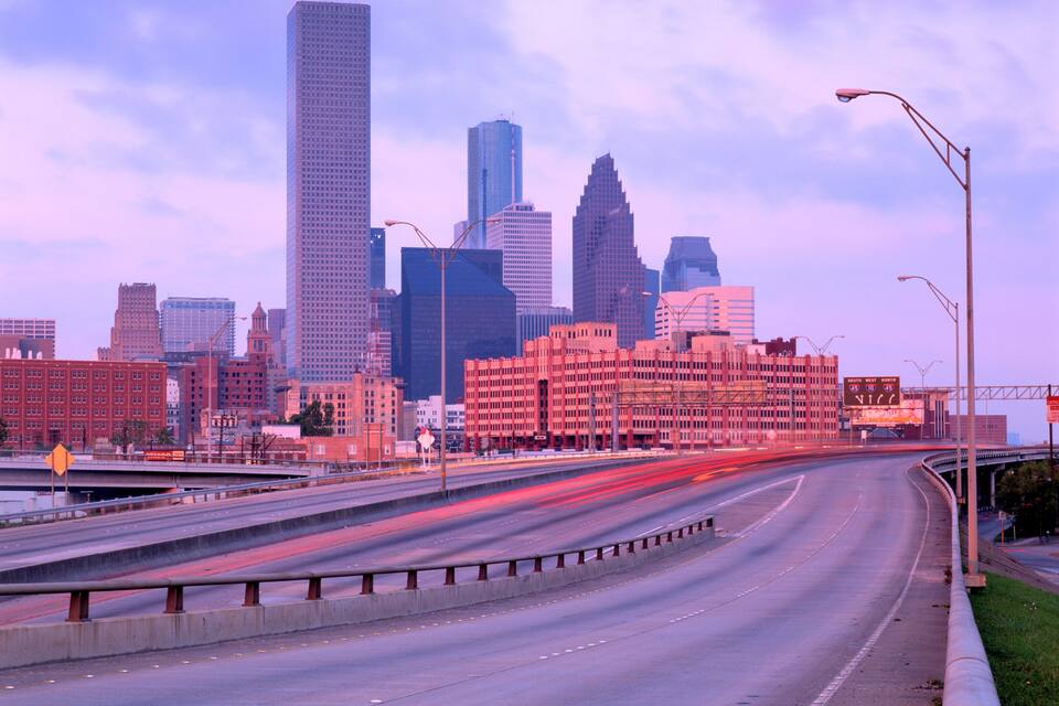 A city skyline with tall buildings and a highway with light trails.