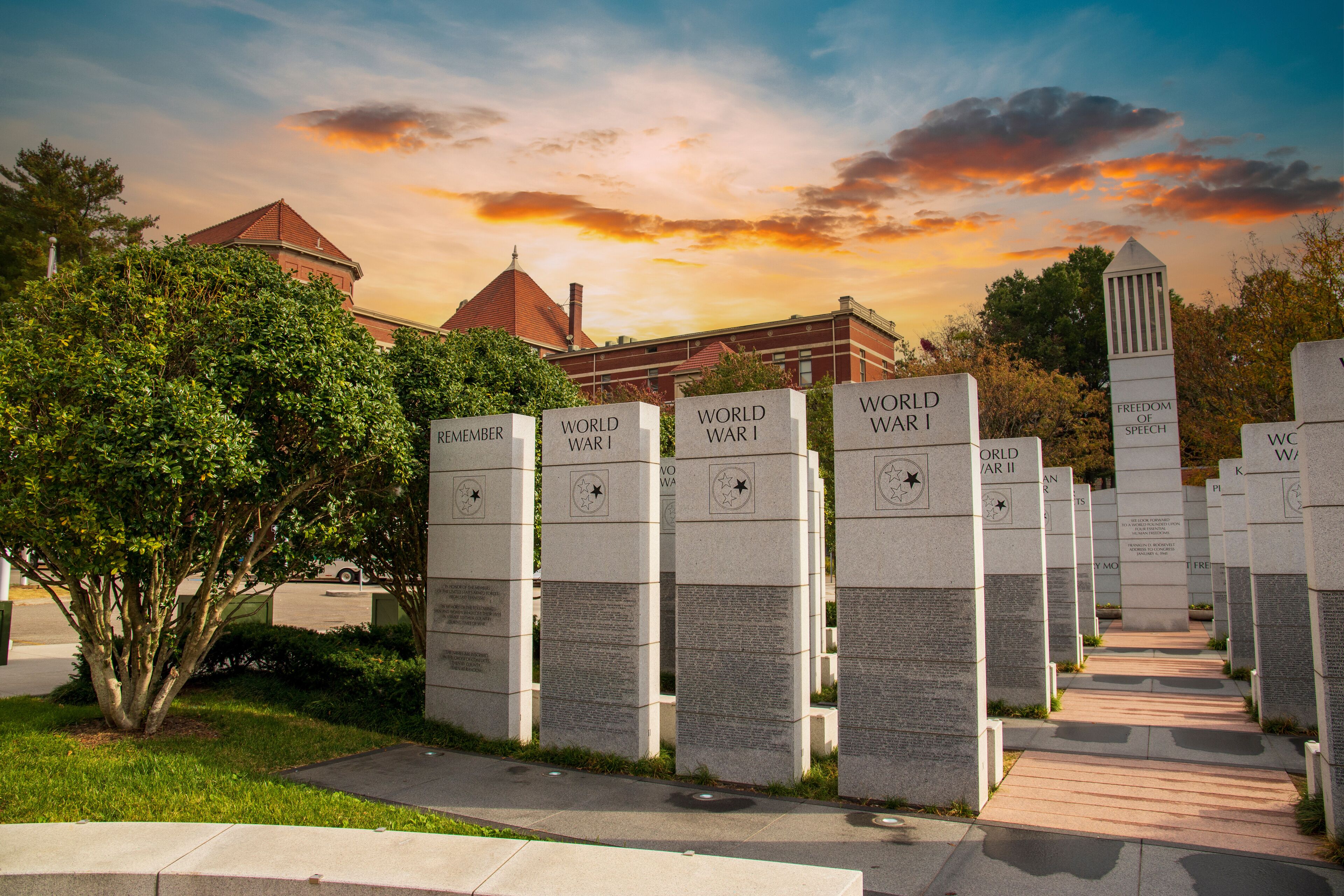 a gorgeous autumn landscape at East Tennessee Veterans Memorial in World's Fair Park with stone slabs surrounded by autumn colored trees and lush green trees and powerful clouds at sunset in Knoxville