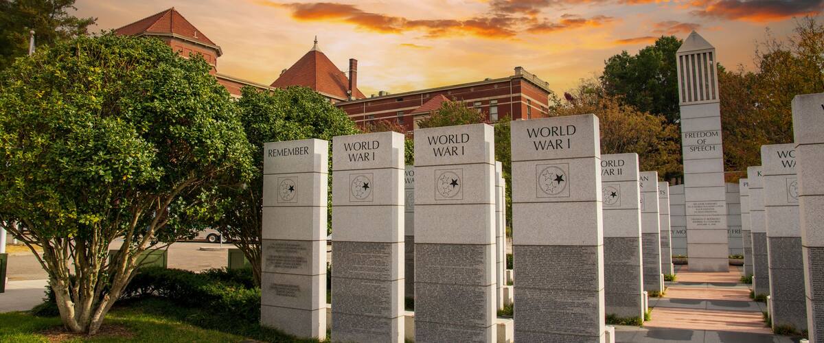 a gorgeous autumn landscape at East Tennessee Veterans Memorial in World's Fair Park with stone slabs surrounded by autumn colored trees and lush green trees and powerful clouds at sunset in Knoxville