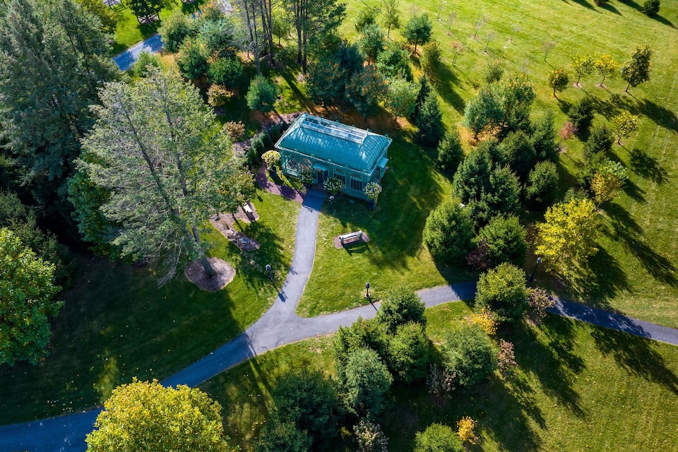 An aerial view of a greenhouses surrounded by a landscaped garden with trees and a winding path.