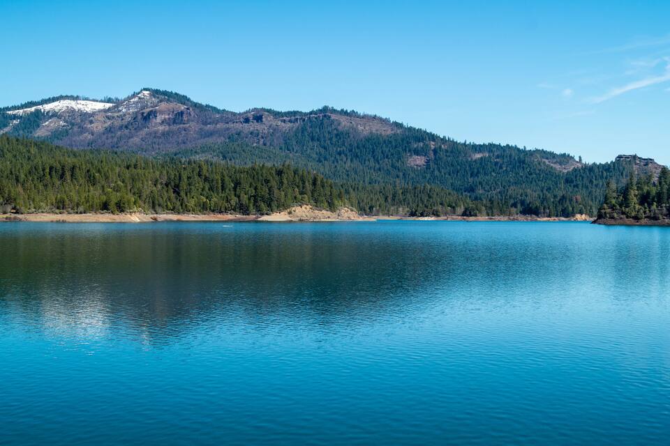 A calm lake with a forested mountain in the background.