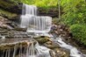 A multi-tiered waterfall surrounded by lush greenery and rocky terrain.