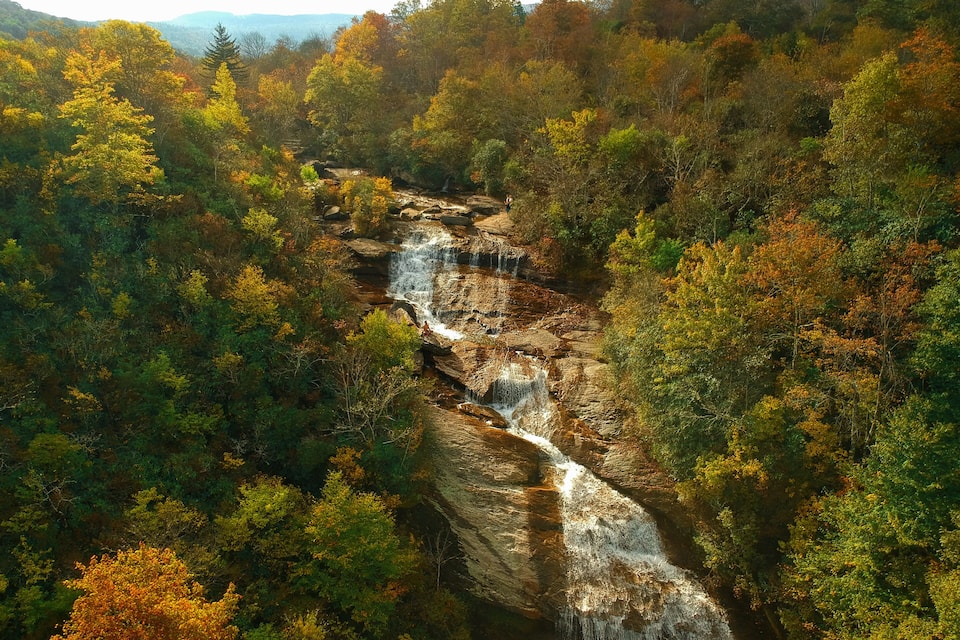 A waterfall cascading through a forested gorge with autumn foliage.