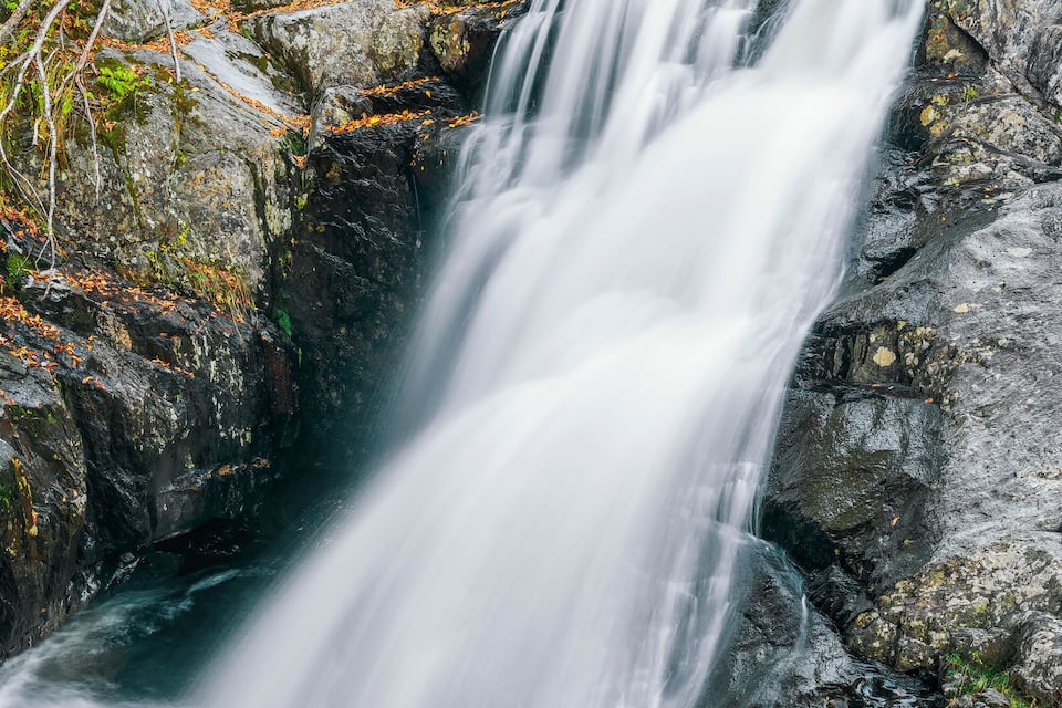 A waterfall cascading over rocks in a forested area with autumn foliage.